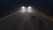 Car with headlights on follows camera tracking along country night road