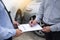 Car insurance agent send a pen to his customers sign the insurance form on clipboard while examining car after accident claim