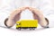 Car insurance. Yellow truck miniature covered by hands.