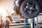 The car is lifted for repair on a lift in a car service station, a mechanic in overalls repairs in the background. Wheel close-up