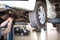 The car is lifted for repair on a lift in a car service station, a mechanic in overalls repairs in the background. Wheel close-up