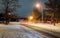 Car light in night on ice road in in the residential area snow falling on the house, night winter time