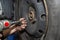 The car mechanic bolts the steel car wheel with a pneumatic wrench in a car workshop, visible male hands.