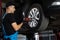 Car mechanic replacing car wheel of lifted automobile at repair service station. Assembly or dismantling of the wheels