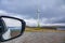 Car mirror with ocean and windmill under cloudy sky