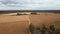 Car moving on countryside rural road among cereal wheat fields and farmhouse