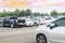 Car parking in large asphalt parking lot with trees, cloud and sky background.