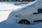 The car in the parking lot is completely covered with snow. Problems after heavy snowfall. Large snowdrifts in the parking lot and