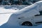 The car in the parking lot is completely covered with snow. Problems after heavy snowfall. Large snowdrifts in the parking lot and