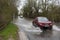 Car passes through flooded road with warning and measuring gauge