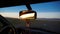 Car rear view mirror. Displays orange dawn. Visible road, hills and steppe.