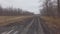 The car rides on a muddy country road on a cloudy autumn day.