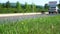 Car rides on road. Blurred background. Close up shot, focused on grass in foreground. Summer day, car traffic in provincial town