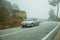 Car in a road passing through wooden landscape with mist