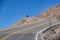 Car rounding sharp bend with steep dropoff on dangerous mountain road with blue sky behind