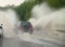 Car runs into big puddle at heavy rain, water splashing over the car. Car driving on asphalt road at thunder storm. Dangerous driv