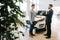 Car salesman handing over keys for new car to young man buyer in auto dealership, in front of car.