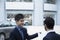 Car salesman holding car keys and paperwork and selling a car to a young businessman