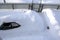Car in a snowdrift near the house, top view. The passenger car was covered with snow. There is a lot of snow outside