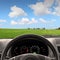 Car steering wheel and dashboard against green wheat field view