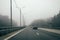 Car traffic on highway with barrier. Fog or haze on road, dangerous cloudy weather for driving vehicle. Freeway in forest in mist