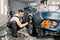 Car washing and detailing photo. Caucasian man worker in protective overalls and rubber gloves, washing car alloy wheel