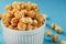 Caramel popcorn in a white glass cup with scissors on a blue background