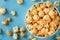 Caramel popcorn in a white glass cup with scissors on a blue background