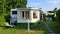 Caravan with a fixed veranda made of awning fabric, glass sliding windows and blinds on a German campsite.