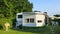 Caravan with a fixed veranda made of awning fabric, glass sliding windows and blinds on a German campsite.