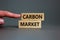 Carbon market symbol. Concept words `carbon market` on wooden blocks on a beautiful grey background, businessman hand. Business