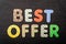 Card with Best Offer words made from mixed vivid colored wooden letters on a textured dark black textile material that can be used