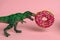 card with dinosaur with open mouth bites strawberry donut on a pink background