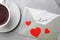 Card with handwritten word love in envelope near cup of coffee on grey table, flat lay