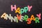 Card with Happy Anniversary words made from mixed vivid colored wooden letters on a textured dark black textile material that can