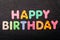 Card with Happy Birthday words made from mixed vivid colored wooden letters on a textured dark black textile material that can be