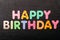 Card with Happy Birthday words made from mixed vivid colored wooden letters on a textured dark black textile material that can be