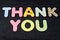 Card with Thank You words made from mixed vivid colored wooden letters on a textured dark black textile material that can be used