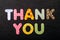 Card with Thank You words made from mixed vivid colored wooden letters on a textured dark black textile material that can be used