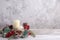 Card of two beige vanilla thick Christmas candles and a wreath of cones, red berries on a wooden background