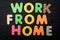 Card with Work from Home words made from mixed vivid colored wooden letters on a textured dark black textile material that can be