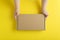 Cardboard box in small childrens hands. Yellow background  top view. Mock up