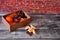 A cardboard box with tangerine and a pine cone lies on a wooden table, next to chocolate wedges and citrus pieces