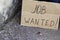 Cardboard plate next to unemployed sitting on concrete with job wanted coins lie nearby on a ground