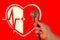 Cardio therapy concept. Hand with stethoscope on red background. Blurred image of heart, medical cross and electrocardiogram.