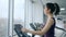 Cardio training, young women does sports on Elliptical trainers in fitness center with large windows