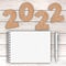 Cardstock Numbers 2022 Happy New Year Sign near White Spiral Paper Cover Notebook with Pen over table. 3d Rendering