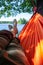 Carefree barefoot man relaxes lying in a hammock in the shade of trees, with a magnificent view of the lake, on a summer