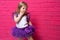 Carefree cute little girl in tutu skirt giggling covering her mouth with her hand on pink background