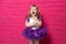 Carefree cute little girl in tutu skirt giggling covering her mouth with her hand on pink background